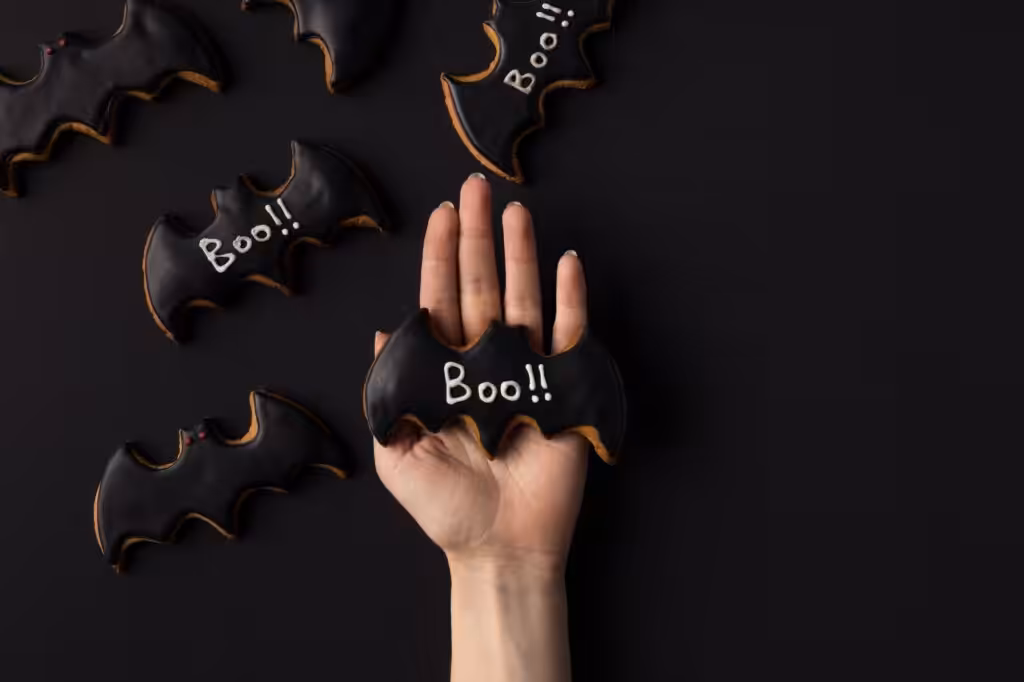 cropped shot of human hand holding halloween cookie in shape of bat